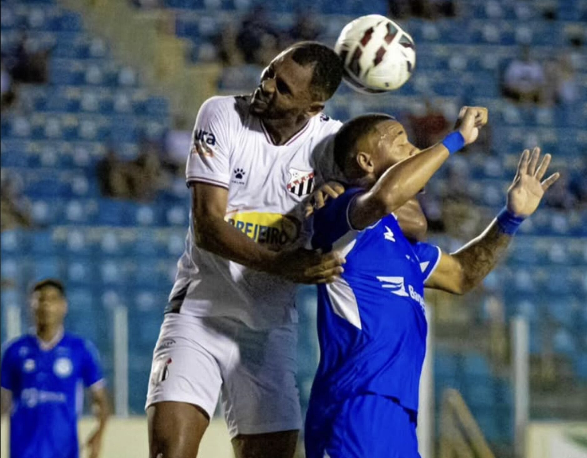 Imagem jogador de branco e azul disputando a bola no alto