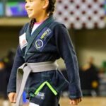 Imagem de uma jovem usando kimono preto e faixa cinza, está no tatame.