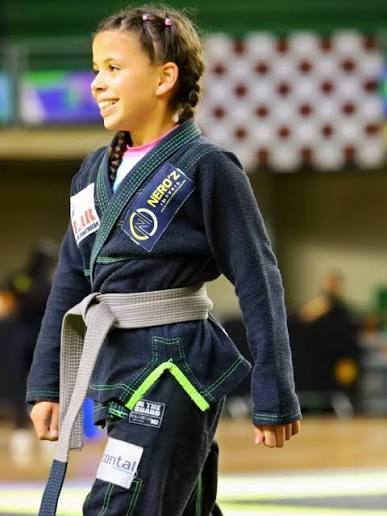 Imagem de uma jovem usando kimono preto e faixa cinza, está no tatame.