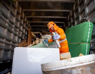 Imagem homem de roupa laranja dentro de caminhão com objetos dentro