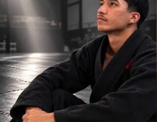 Imagem de um jovem usando kimono preto, olhando para cima, sentado no chão.