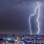 Imagem de raios no céu escuro em Goiás, algumas casas e prédios com luzes acessas abaixo.