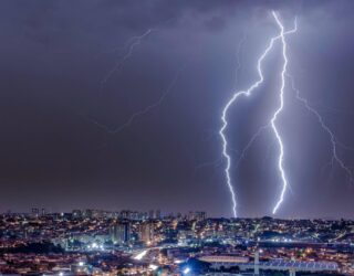 Imagem de raios no céu escuro em Goiás, algumas casas e prédios com luzes acessas abaixo.