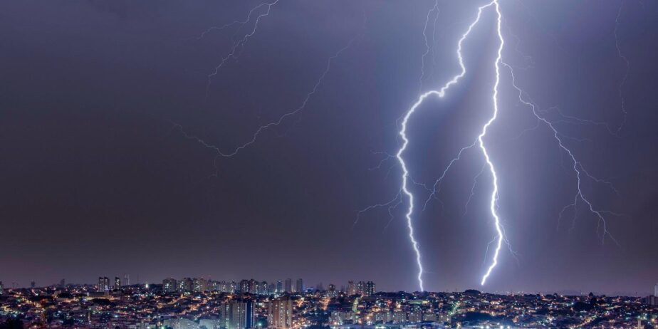 Imagem de raios no céu escuro em Goiás, algumas casas e prédios com luzes acessas abaixo.