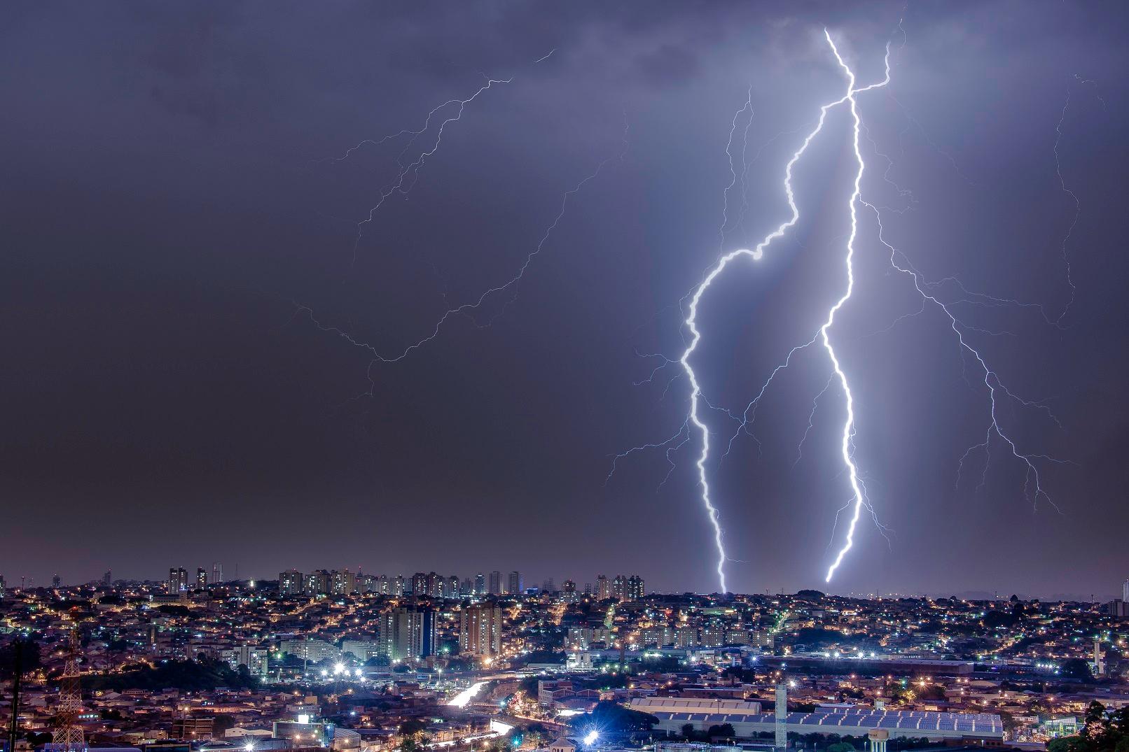 Imagem de raios no céu escuro em Goiás, algumas casas e prédios com luzes acessas abaixo.