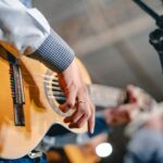 Imagem de um homem tocando viola, na imagem aparece apenas os braços e mãos do homem.