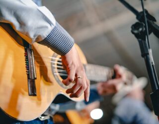 Imagem de um homem tocando viola, na imagem aparece apenas os braços e mãos do homem.