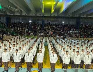 Imagem de alunos de Colégio Militar em posição de sentido em uma quadra da escola, vestindo farda branca.