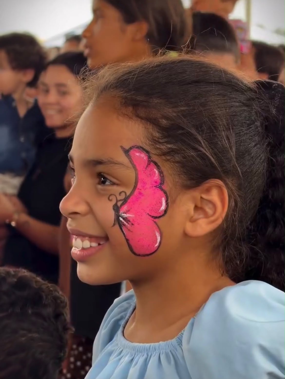 Imagem, criança sorridente com uma borboleta rosa pintada em um lado do rosto.