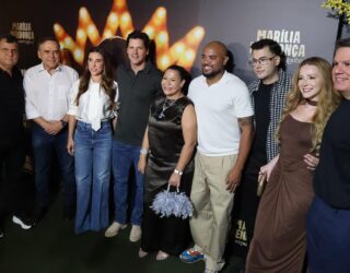 Imagem do governador, sua esposa e amigos pousando para fotos. Atrás um painel lançamento de série documental sobre Marília Mendonça