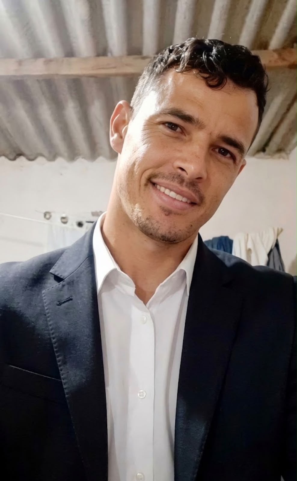 Imagem de um homem, usa camisa branca e blazer preto, sorri para a foto.