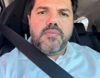 Imagem do Prefeito Márcio Corrêa, usando camisa azul clara, dentro do carro, o cinto de segurança transpassado.