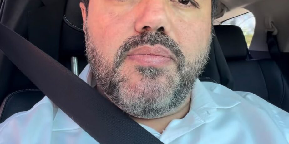 Imagem do Prefeito Márcio Corrêa, usando camisa azul clara, dentro do carro, o cinto de segurança transpassado.