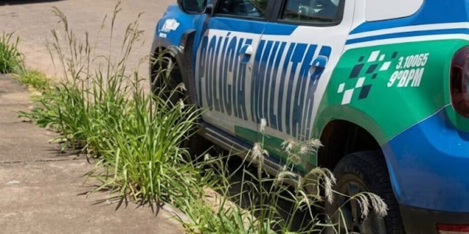 Imagem de uma viatura da Polícia Militar estacionando na porta de uma casa. Na calçada alguns matinhos e a frente outro carro estacionado.