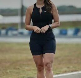 Imagem da Delegada Aline Lopes, com roupa preta, tênis de corrida e meia, mãos entrelaçadas, olhando para frente, com cabelos soltos, em uma pista de corrida.